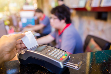 Hand put credit card In slot of credit card reader with blurry cashier and customer at counter service, credit card payment, buy and sell products & service, the concept of payment, selective focus.