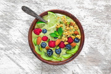 green smoothie bowl made of matcha tea with fresh fruits, berries, nuts, seeds with a spoon for healthy vegan breakfast