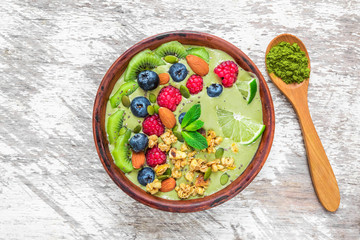 Smoothie bowl made of matcha green tea with fresh fruits, berries, nuts, seeds with a spoon