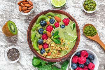 healthy vegan breakfast. matcha green tea smoothie bowl with fresh fruits, berries, nuts, seeds and granola. top view