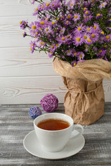 Romantic background with a cup of tea, lilac flowers in a vase on a gray wooden table