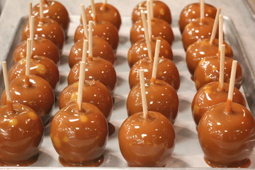 shiny fresh caramel apples with sticks on a metal baking sheet 