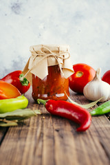Adjika in a jar on a wooden background, spicy tomato sauce