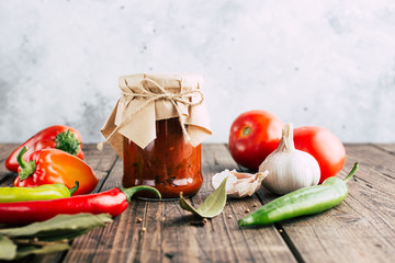 Adjika in a jar on a wooden background, spicy tomato sauce