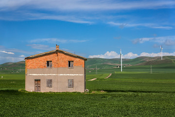 Fototapeta na wymiar Old House in Field with Wind Turbines