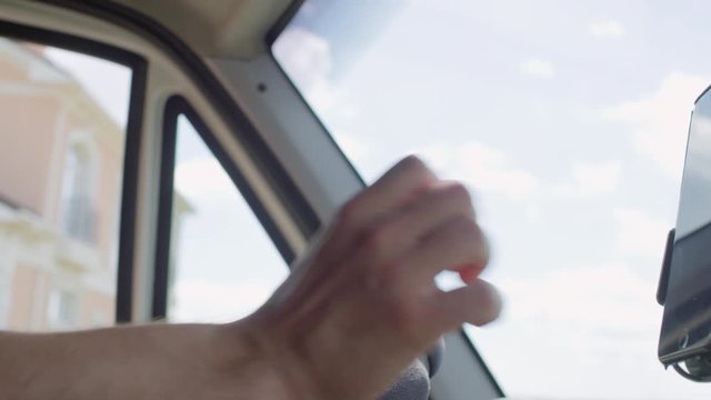 Handheld shot with close up of hands of unrecognizable male courier driving delivery van and checking navigation on mobile phone