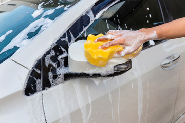 Woman hand with yellow sponge washing side mirror modern car or cleaning automobile. Car wash...