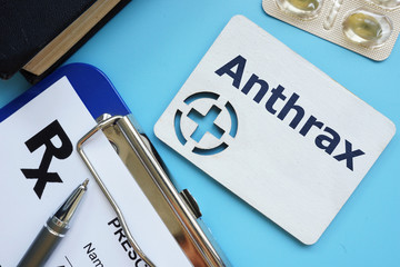Writing note showing Anthrax. The text is written on a small wooden board with red cross silhouette. There are pills, blister, table on the photo.