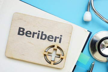 Writing note showing Beriberi. The text is written on a small wooden board with red cross silhouette. There are book, stethoscope, pen, blue table on the photo.