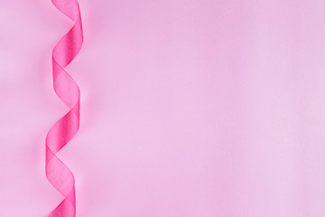 Festive pink satin silk organza ribbon spiral on pink background. Holiday decoration. Present...