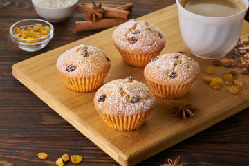 Homemade fresh muffins with sugar powder and coffee cup on rustic wooden table background.