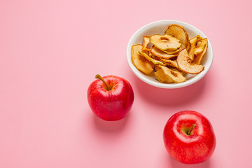 Dried apples chips in ceramic bowl with fresh red apples on table