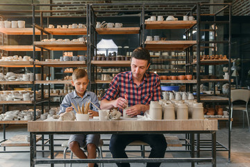 Little cute boy with his father making ceramic pots in the pottery.