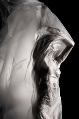 Slim girl dressed only in underwear emotionally posing, wrapped in fluttering in the wind and fitting her graceful young body cellophane film. Artistic, creative, abstract design. Black and white