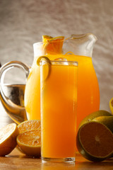 Glass of orange juice served in tall glass with slices of lemon and ice.