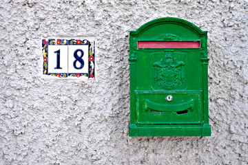 A green letter box and number 18 on a gray wall.