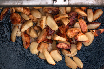 frying potatoes with open fire from coals on a metal disk in oil