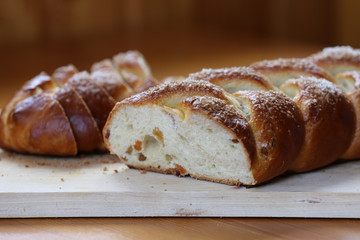 Appetizing baked sweet bun with raisins in the form of a pigtail with sugar on a wooden board.
