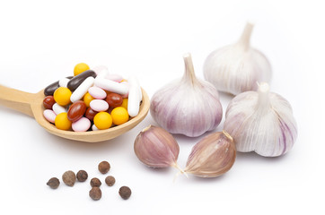 Choice: folk remedy or medicine. Fresh garlic helps to lose weight. Yellow, black, brown and white pills and garlic on a white background