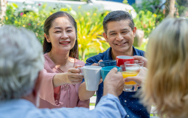 Happy couple senior clinking glasses with their family while breakfast together at home garden