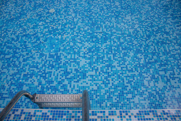 Close up of a blue hotel Swimming pool with blue mosaic tiles of the pool and ladder going down to the water.