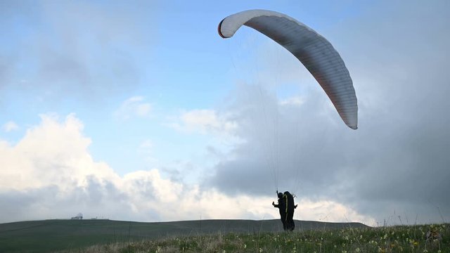 A male athlete paraglider raises a wing in an outdor against the backdrop of evening clouds but cannot fly. Failure while trying to take off