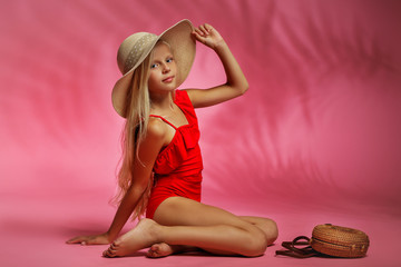 cute fashion little child girl in a red swimsuit and hat posing on a pink background. summer time