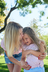 mom and daughter cuddle and smile in the park