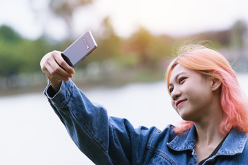 Portrait happy teenage woman taking selfie photo in park.