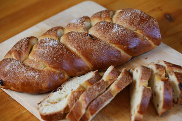 Appetizing baked sweet bun with raisins in the form of a pigtail with sugar on a wooden board