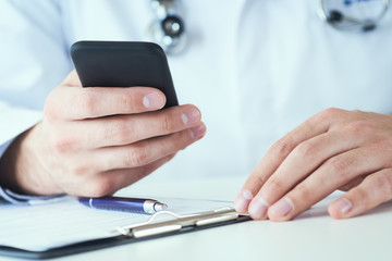 Male doctor hands with mobile phone close-up. Male doctor in white coat is using a modern smartphone device with touch screen.