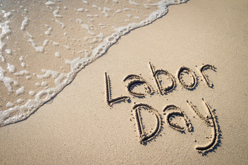 Labor Day message handwritten on the smooth sand of an empty beach with an oncoming wave