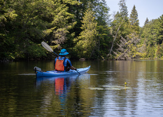 Fototapeta na wymiar Mature man kayaking through a calm creek past evergreen forest and lilies