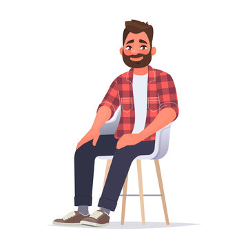 Bearded smiling man dressed in casual clothes is sitting on a chair on a white background