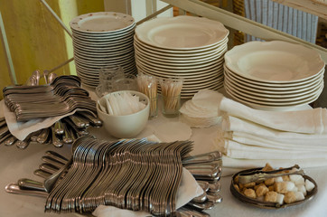 Piles of white clean plates, table knives, forks, spoons, napkins. Preparing for guest service in the restaurant