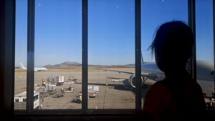 Silhouette of a child watching airplanes from the airport window