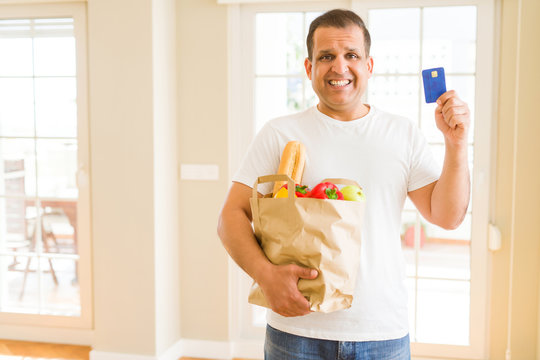 Middle age man holding groceries bag and showing credit card
