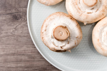 Close-up of white mushrooms on a white plate on a dark wooden table. Vegetarian healthy food