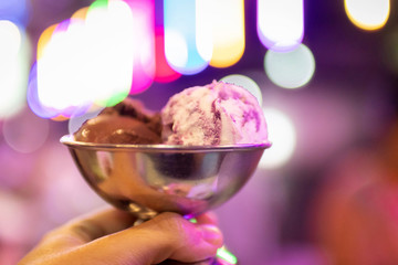 Hand holding a retro metal bowl of ice cream with a bokeh of festive party lights on background.