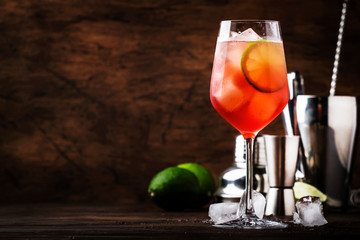 Campari tonic alcoholic cocktail with red bitter, tonic, lime and ice. Old wooden table background,...
