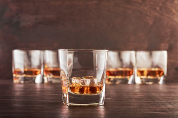 A glass of whiskey on a wooden table. Four whiskies in the background.