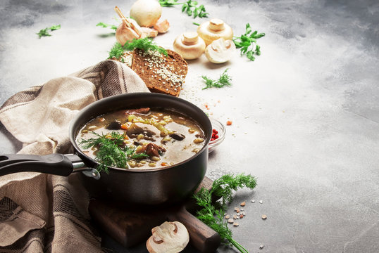 Autumn or winter meat vegetable mushroom hot soup with beef and wholegrain barley. With black breaв and parsley, top view, gray kitchen table, copy space