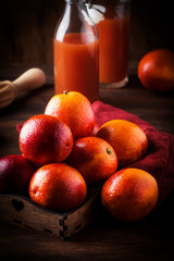Juicy ripe shiny red bloody oranges in tray for making refreshing cocktail on rustic wooden table background, still life, selective focus
