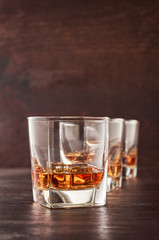Three glasses of whiskey on the ice on the wooden table.