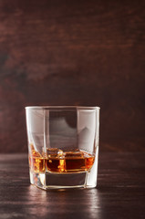 A glass of whisky with ice on a wooden table.