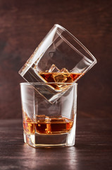 Two glasses of whisky with ice on a wooden table. One glass stands on the other.