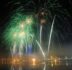 Céu cheio de fogo de artifício em cores verde e ouro com reflexo no rio