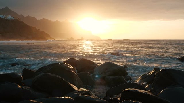 Ocean waves crash on rocks and spray in beautiful sunset light at Benijo beach in Tenerife, Canary Islands.