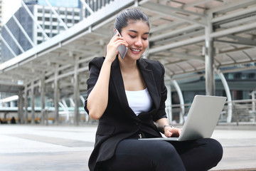 Attractive young Asian business woman working with laptop and mobile smart phone at outside office.
