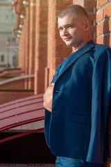 Young handsome sporty man in a blue business suit on a background of a brick wall in the summer.